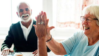 Fotografia donde se encuentran compartiendo un grupo de adultos mayores y dos de ellas chocan felices las manos