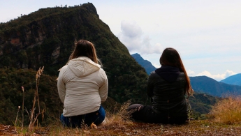 Dos mujeres de espaldas sentadas apreciando una montaña de fondo