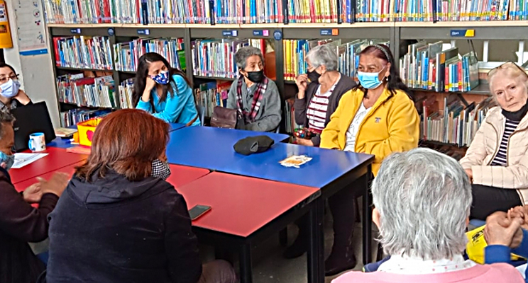 Fotografía de un grupo de señoras de la tercera edad compartiendo un diálogo en la biblioteca.