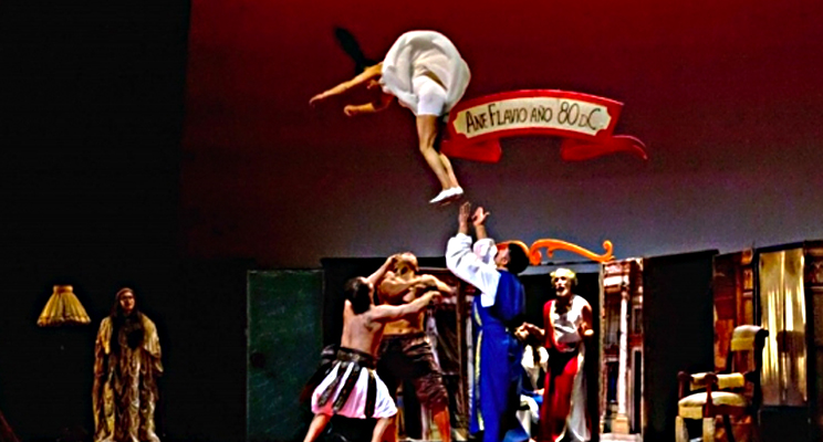 Fotografía de un fragmento de la obra "Las 7 maravillas" en la cual una actriz se encuentra en el aire mientras un grupo la espera para atraparla.