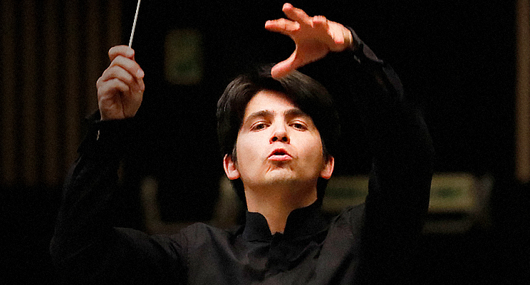 Fotografía en donde se encuentra la cara de un director de orquesta gestualizando con su rostro y sus manos en torno en virtud a la dirección de sus músicos