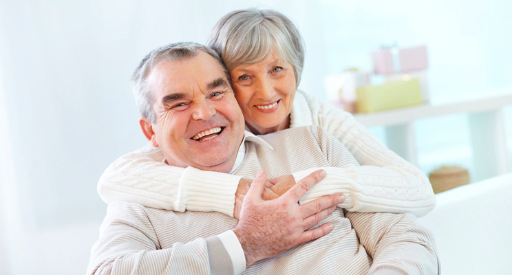 Fotografía de una pareja de la tercera edad abrazados mirando hacia el frente y ambos sonriendo de felicidad.