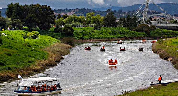 Fotografía de una parte del río Bogotá a la altura del puente de guadua por la calle 80 en la cual se ven diferentes lanchas transportando turistas sobre el lecho del río.