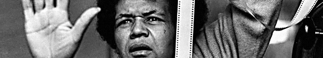 Parte de un fotograma de una película de Sarah Maldoror, donde sale ella tomando una película de 35mm, con su mano izquierda en expresión de ¡Para! y su rostros con gesto dramático