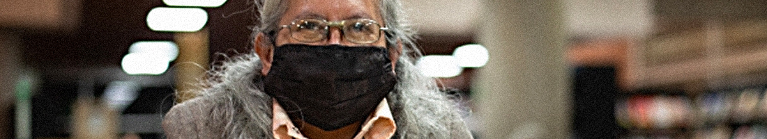 Foto en primer plano de una señora de la tercera edad con gesto de sonrisa y tapabocas en la biblioteca