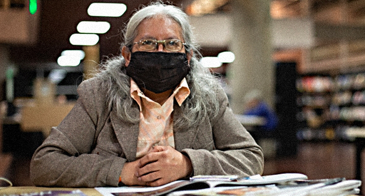 Foto en primer plano de una señora de la tercera edad con gesto de sonrisa y tapabocas en la biblioteca