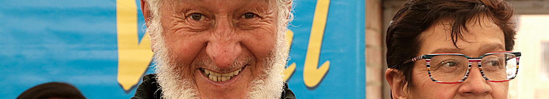 Fotografía de dos adultos mayores, un hombre con barba blanca y una mujer con gafas, sonriendo
