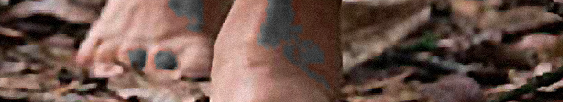 Fotografía en primer plano de unos pies descalzos caminando sobre hojarasca.