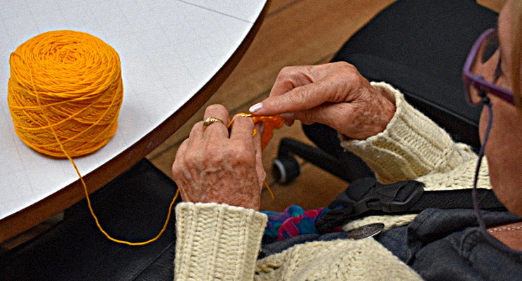 Fotografía de una señora de la tercera edad tejiendo con lana de color amarillo