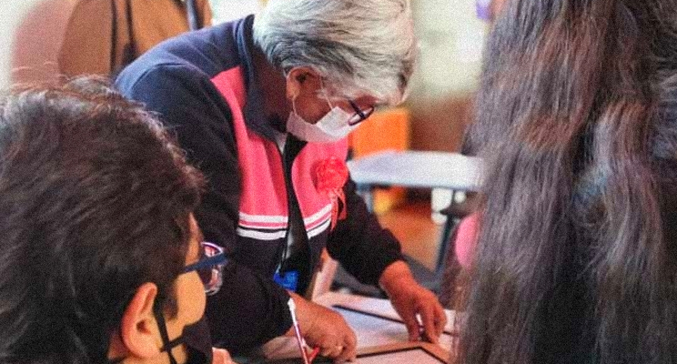 Señora de la tercera edad con gafas mirando hacia abajo y trabajando sobre una mesa acompañada e otras señoras