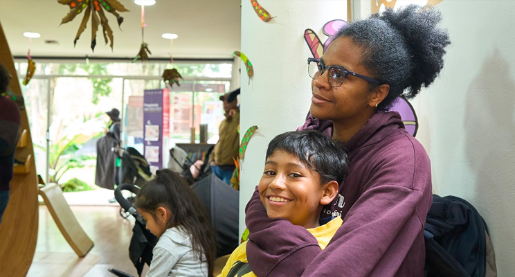 En la foto una mujer afro con gafas apreciando algo con mucha atención y en sus brazos un niño sonriendo