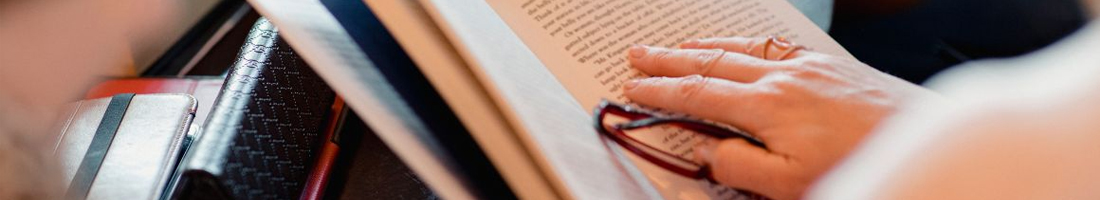 Persona sosteniendo libro con gafas de lectura