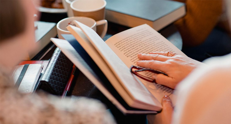 Persona sosteniendo libro con gafas de lectura