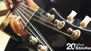 Primer plano de la cabeza de una guitarra acústica y unas manos tocando las cuerdas - Texto 20 años BibloRed