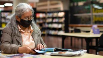 Adulta mayor con tapabocas leyendo en la biblioteca