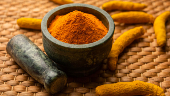 Fotografía de unas raíces de curcuma maceradas en un mortero de piedra oscura sobre una estera