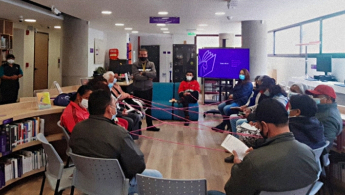 Fotografía de un grupo de adultos mayores en un espacio de taller en la biblioteca, interactuando por medio de hilos.
