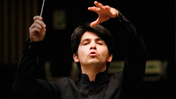 Fotografía en donde se encuentra la cara de un director de orquesta gestualizando con su rostro y sus manos en torno en virtud a la dirección de sus músicos