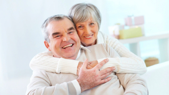 Fotografía de una pareja de la tercera edad abrazados mirando hacia el frente y ambos sonriendo de felicidad.