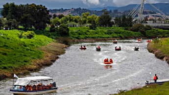 Fotografía de una parte del río Bogotá a la altura del puente de guadua por la calle 80 en la cual se ven diferentes lanchas transportando turistas sobre el lecho del río.