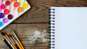 Fotografía en primer plano de una paleta de acuarelas, unos pinceles y una libreta de bocetos en blanco