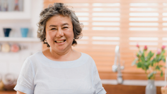 Fotografía de una señora de la tercera edad sonriendo muy contenta en su cocina