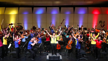 Fotografía de la orquesta completa levantando la mano y con rostros de felicidad