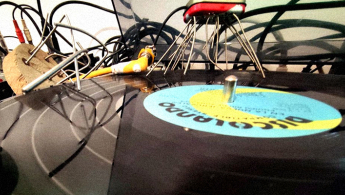 Fotografía de un disco de vinilo junto a un tornamesa y cables al fondo