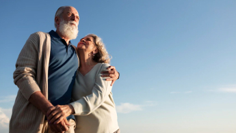 Fotografía de una pareja de la tercera edad abrazados y sonriendo mirando hacia el futuro