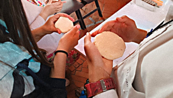 Fotografía de unas manos adultas y otra jóvenes amasando arepas.