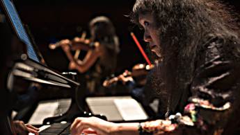 Foto de una mujer interpretando el teclado y mirando su partitura en una tableta digital.