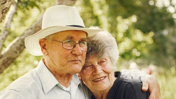 Dos adultos mayores (Mujer y Hombre) abrazados con expresión de tranquilidad y felices.