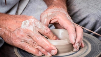 Manos de un adulto mayor sobre un torno modelando una figura de cerámica