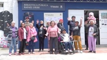 Grupo de personas adultas mayores sonriendo y saludando en la entrada de la Biblioteca Pública Rafael Uribe Uribe