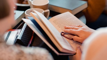 Persona sosteniendo libro con gafas de lectura