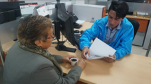 Un hombre joven atendiendo en una oficina a una mujer de la tercera edad.