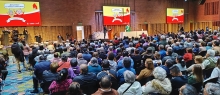 Muchas personas reunidas en auditorio con pantallas gigantes