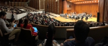Muchas personas en auditorio y orquesta filarmónica en tarima