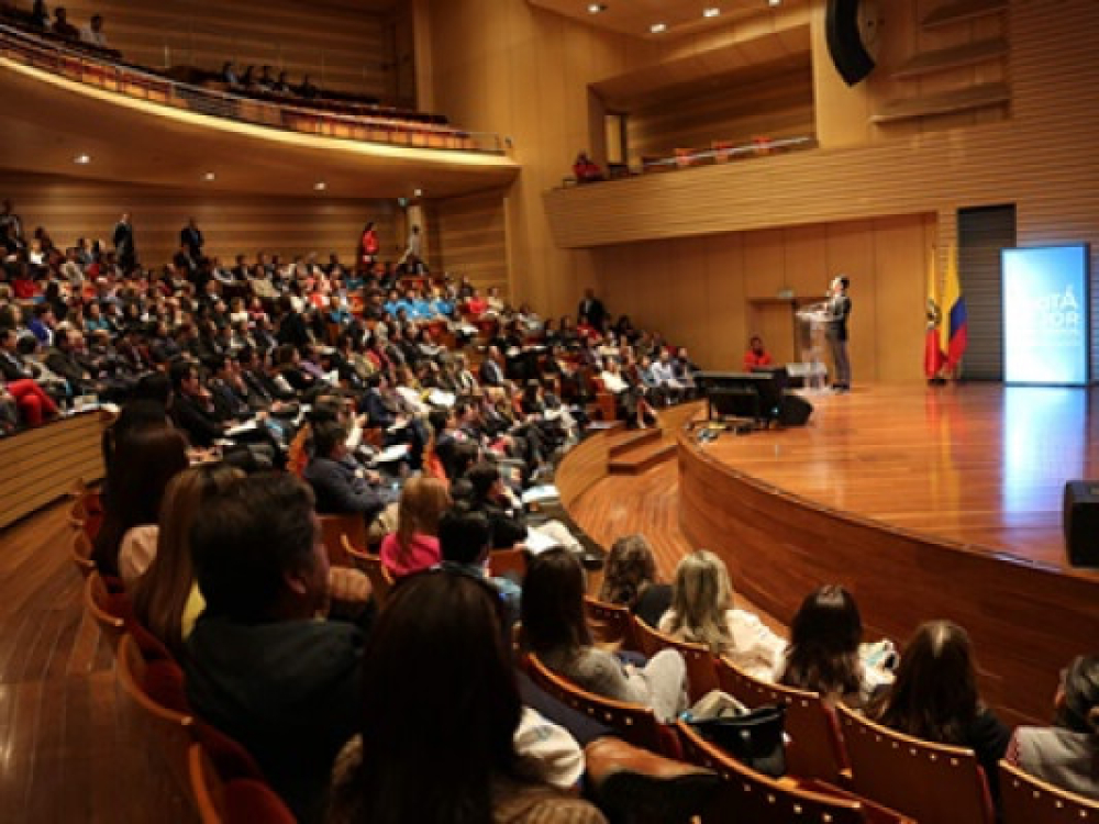 Auditorio con público y un hombre en tarima hablando.