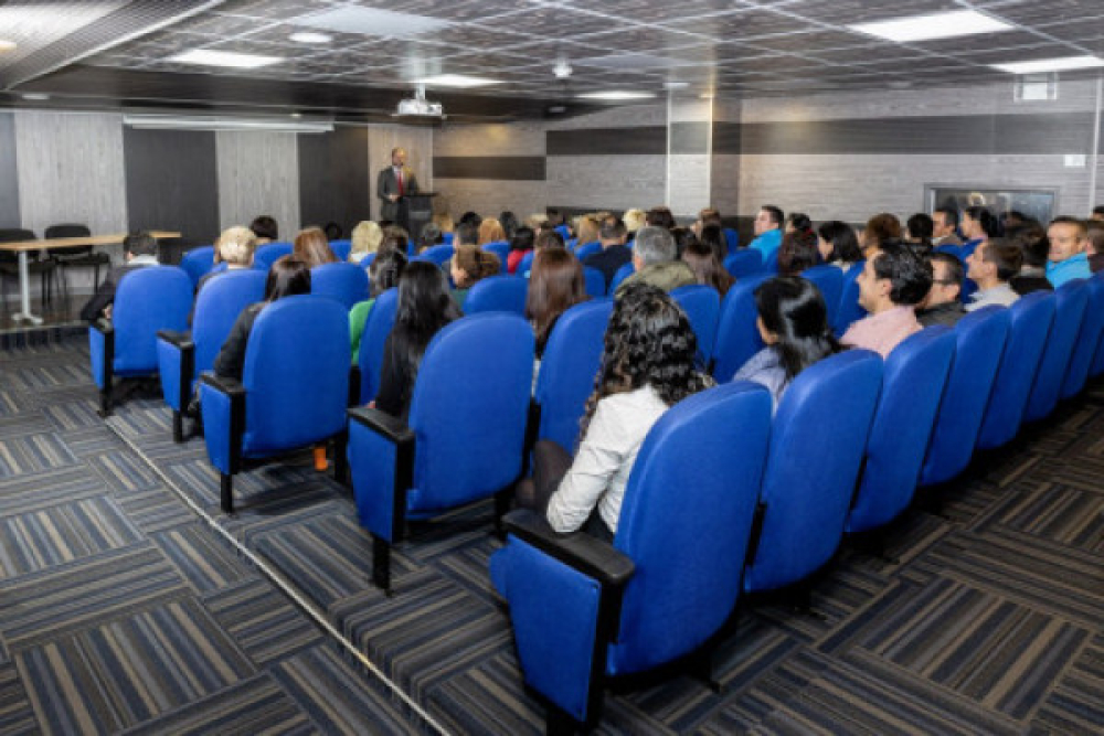 Auditorio con sillas azules y todas ocupadas por personas