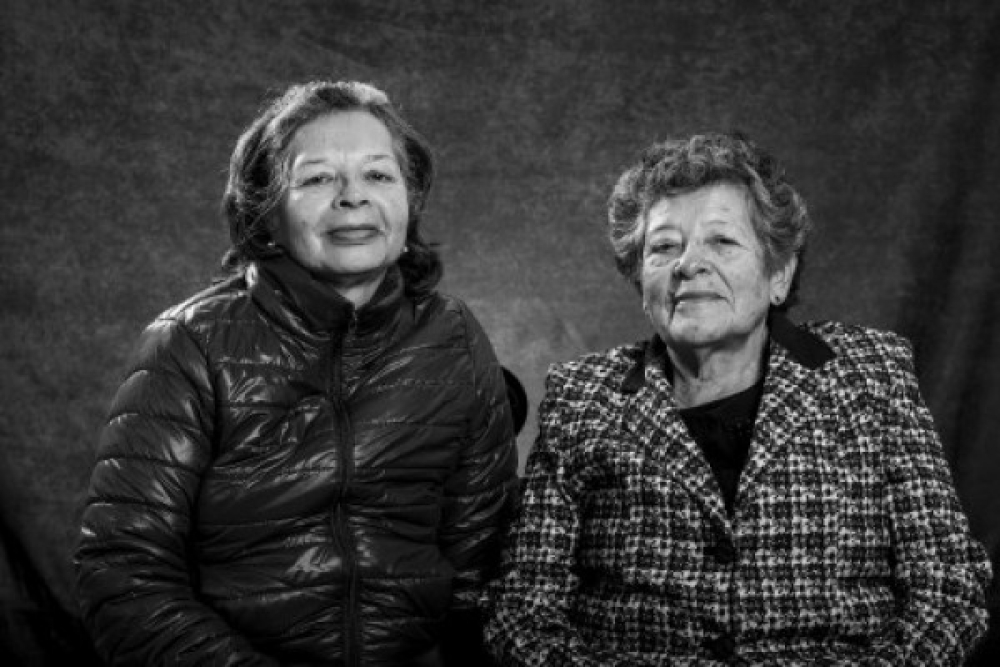 Dos mujeres de la tercera edad, mirando hacia el frente, sonriendo sutilmente.