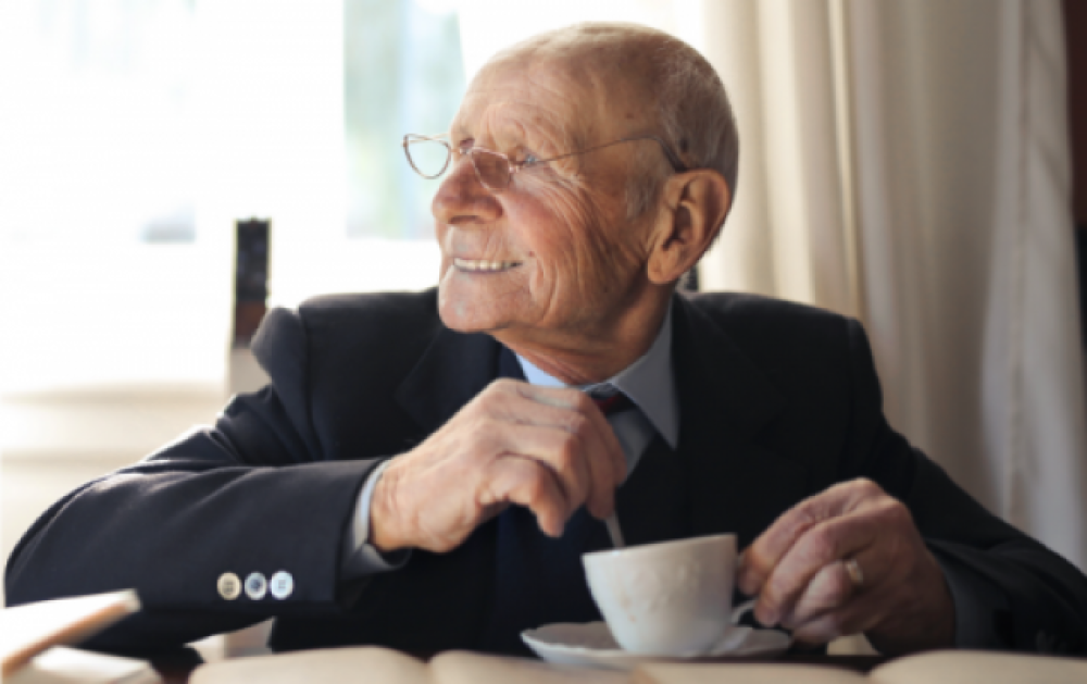 Hombre de la tercera edad, sentado, mirando hacia el horizonte y sosteniendo una cuchada y un pocillo