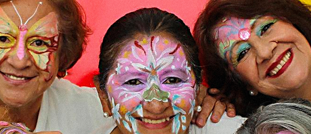 Fotografía de tres mujeres de la tercera edad con maquillaje de carnaval sonriendo.