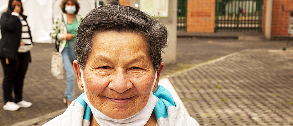 En la fotografía en primer plano una señora de la tercera edad sonriendo.