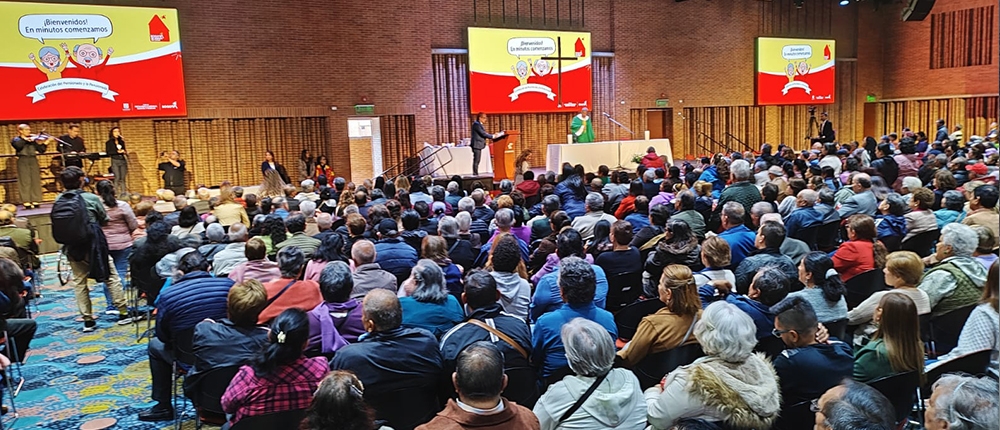 Muchas personas reunidas en auditorio con pantallas gigantes