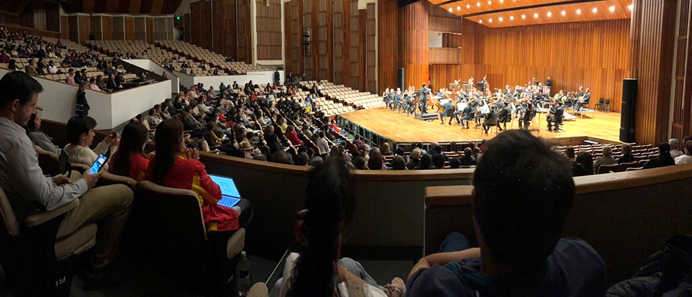Muchas personas en auditorio y orquesta filarmónica en tarima
